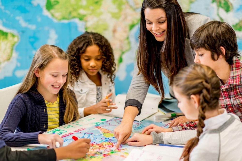 professora e crianças em volta de uma mesa apontam para um mapa.