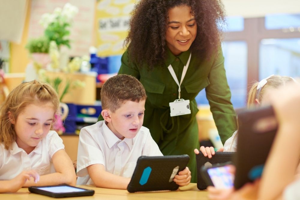 professora auxiliando alunos em atividades com tablets na sala de aula.