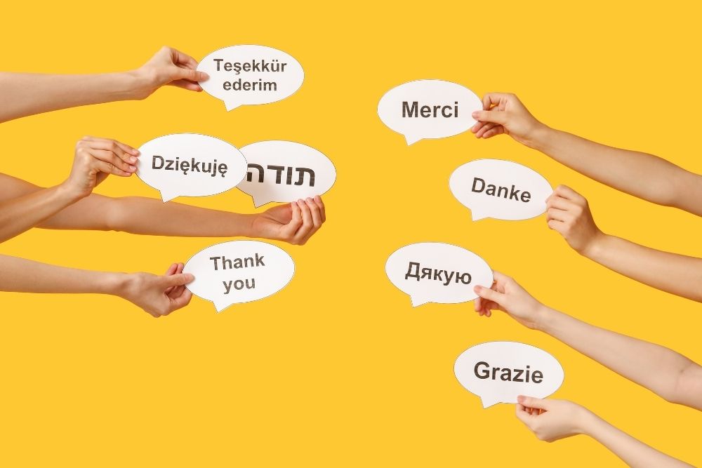 mãos segurando balões de fala com a palavra “obrigado” escrita em diferentes idiomas, como inglês, francês, alemão, italiano.