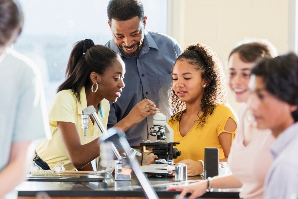 professor auxiliando alunos em um experimento de ciências em laboratório.