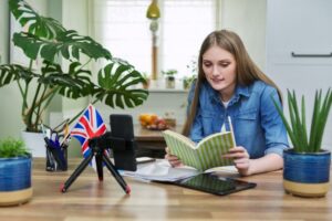 jovem estuda inglês online com livros e bandeira do Reino Unido na mesa.