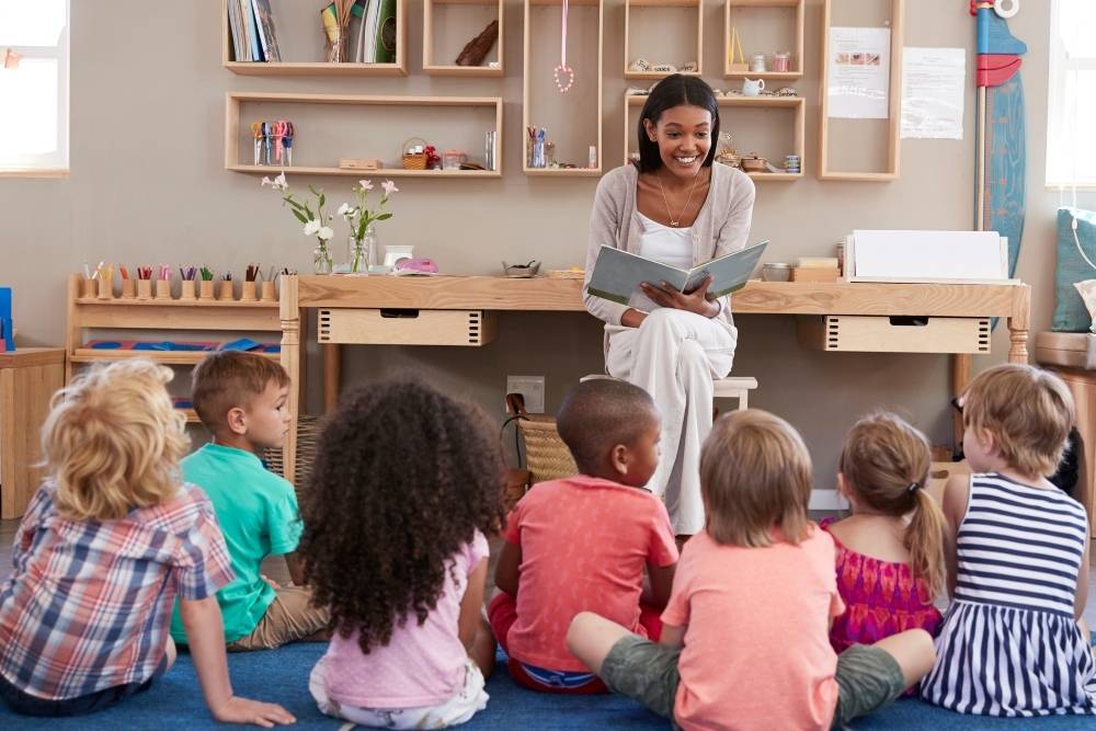 Professora lendo livro em inglês para crianças em roda durante atividade de leitura infantil em sala de aula.