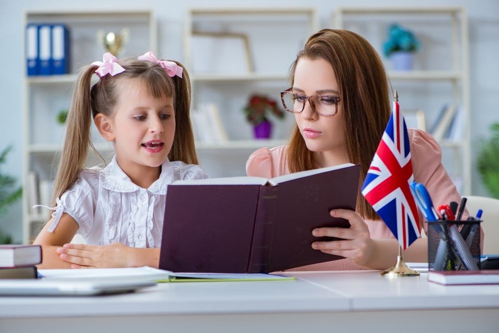 professora e aluna lendo livro de inglês com bandeira do Reino Unido.
