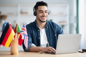 jovem com fones de ouvido estudando idiomas no notebook com bandeiras na mesa.