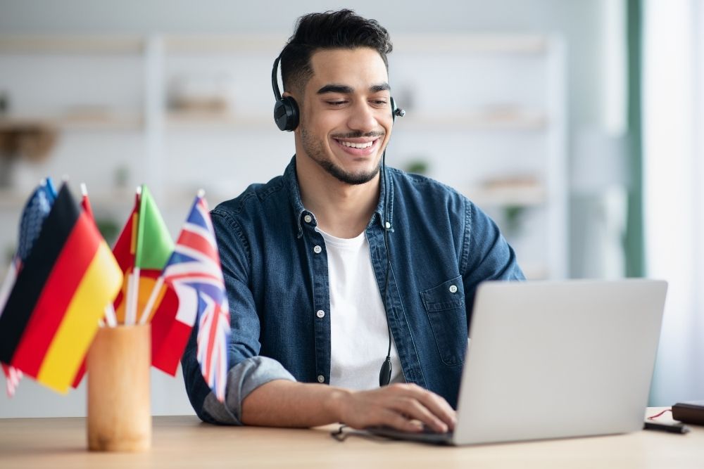 jovem com fones de ouvido estudando idiomas no notebook com bandeiras na mesa.