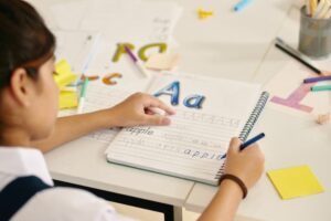 criança escrevendo a palavra “apple” em caderno de caligrafia.